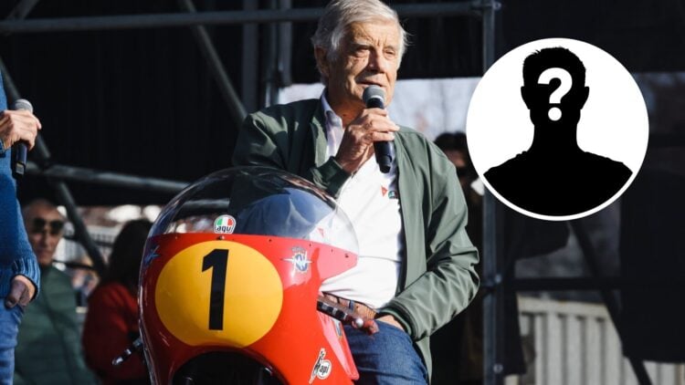 Giacomo Agostini speaking into a microphone at a motorcycle event in Milan.