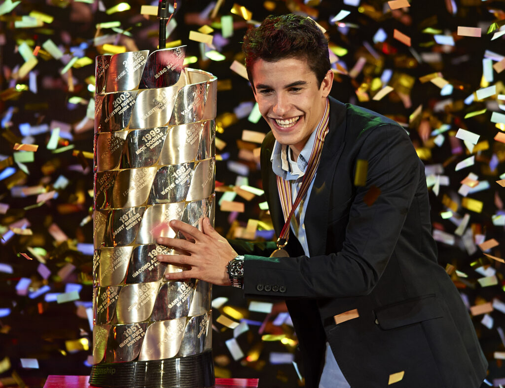 Marc Marquez smiles as he holds the 2013 MotoGP World Championship trophy as confetti falls around him