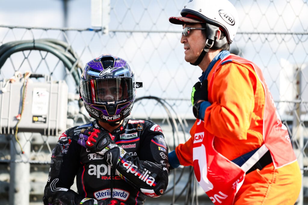Jorge Martin of Aprilia sits with a marshal after a crash at the 2025 Japanese Grand Prix