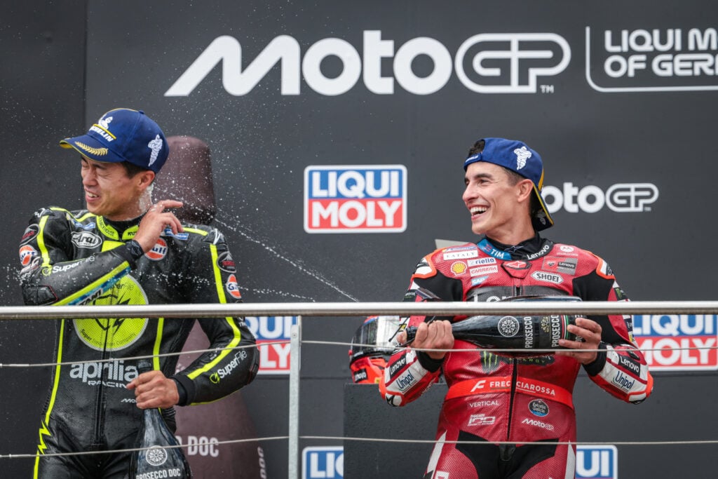 Marc Marquez of Ducati sprays Ai Ogura of Trackhouse Aprilia on the podium of the German Grand Prix.